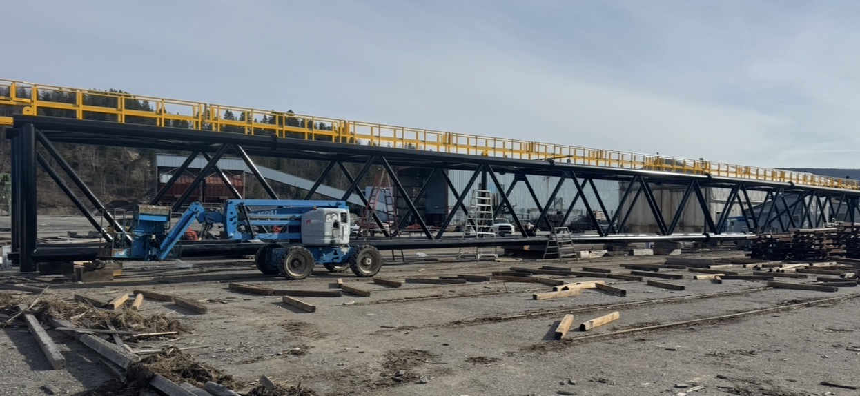 Coated steel truss with yellow handrails on a job site